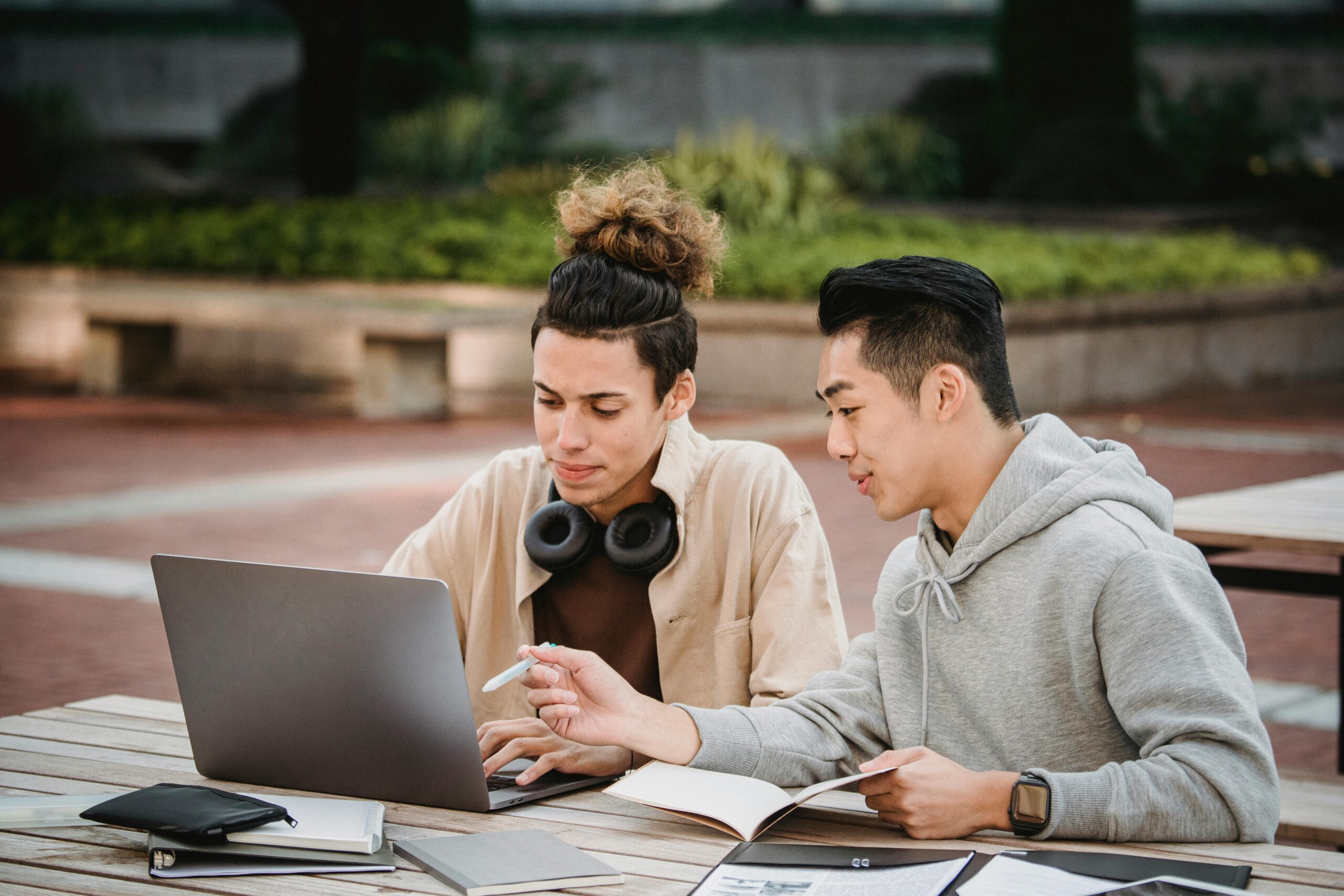 Serious young diverse male students in casual wear sitting at table with laptop and documents while working together on homework