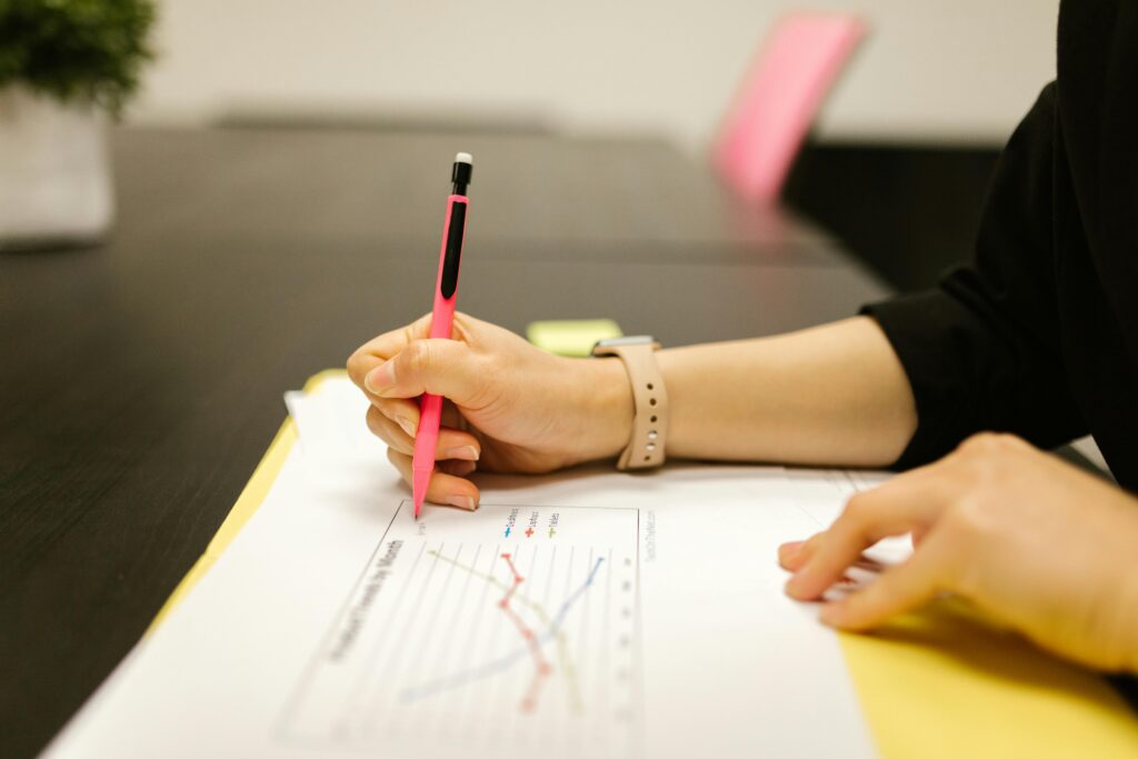 Person writing on a document with a pen, highlighting graph analysis.