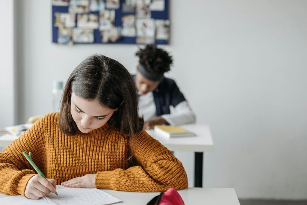 Two students concentrated on writing during class in a bright classroom setting.