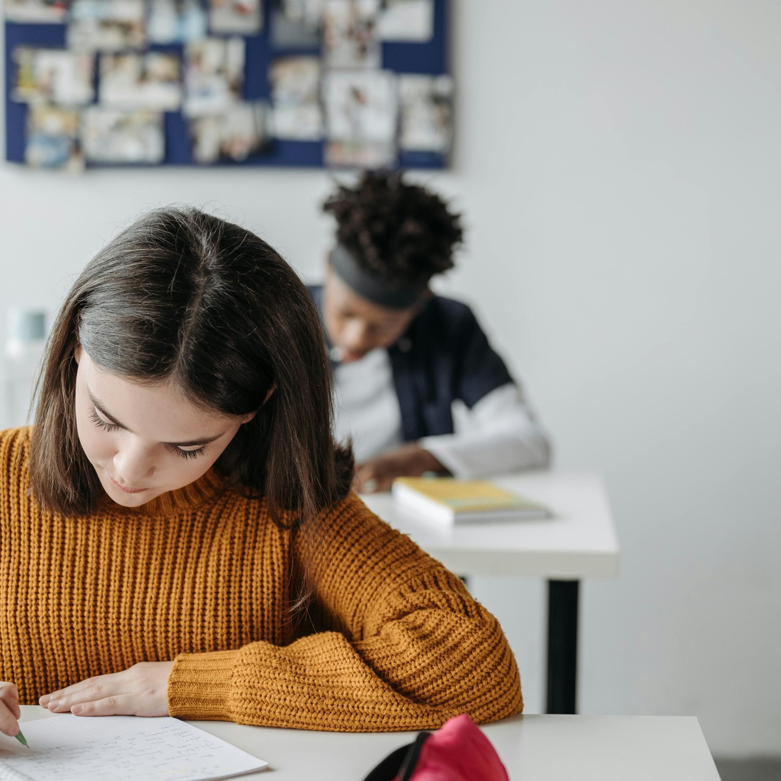 Two students concentrated on writing during class in a bright classroom setting.