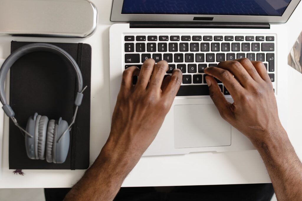 Overhead view of hands typing on a laptop keyboard with headphones nearby.